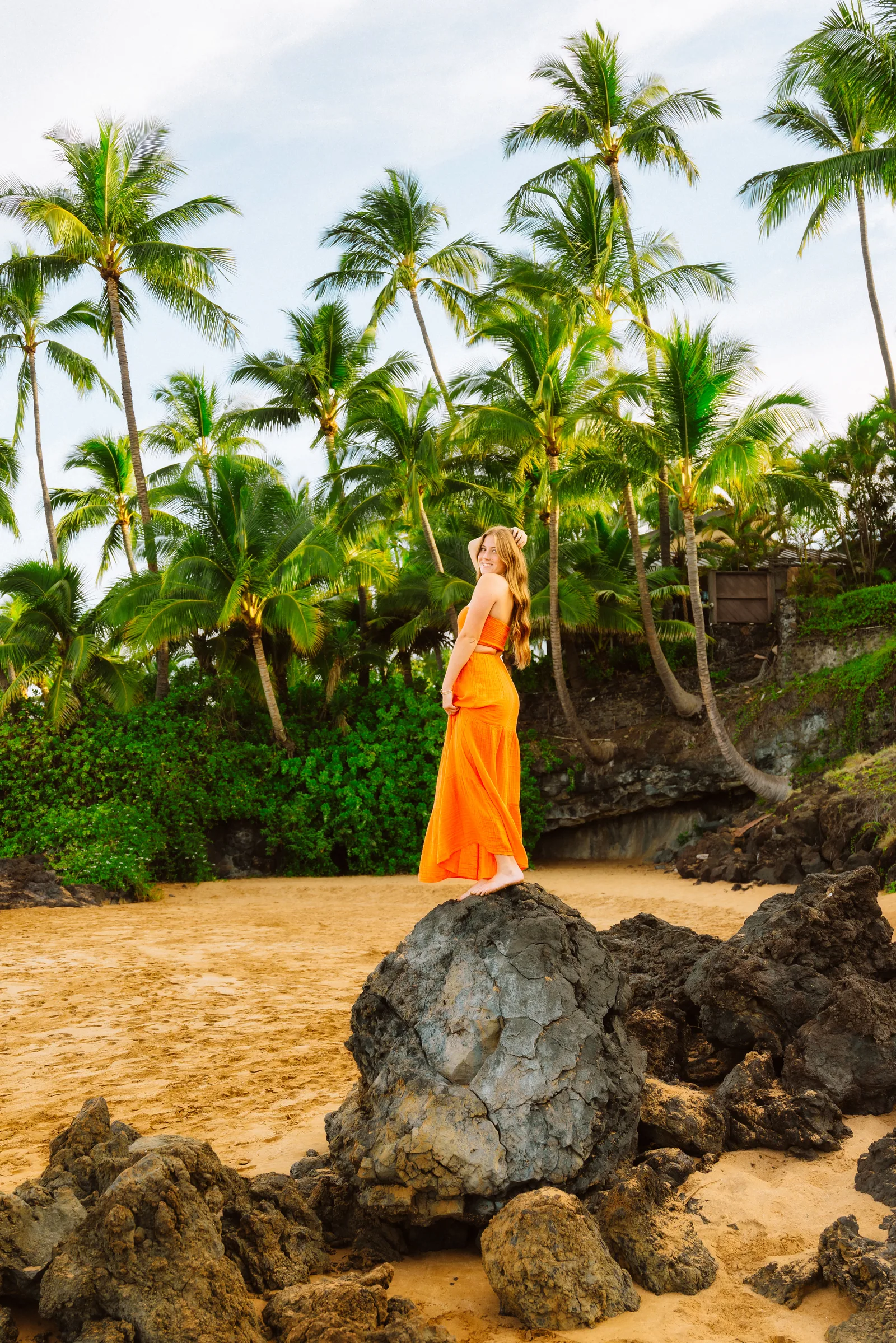 A senior portrait on lava rock with palms rising behind