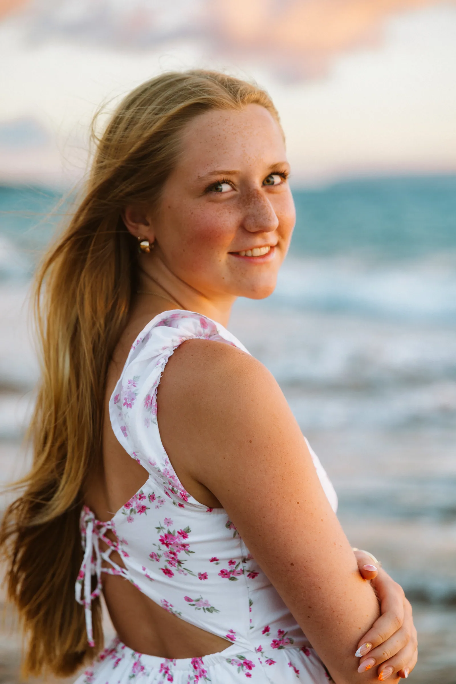 A senior portrait looking back over her shoulder, ocean behind