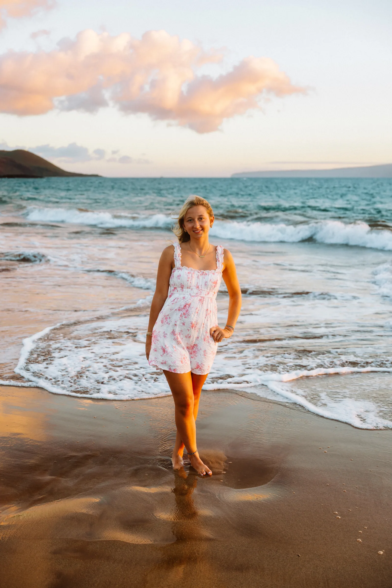 A senior portrait at the water's edge under a pastel evening sky