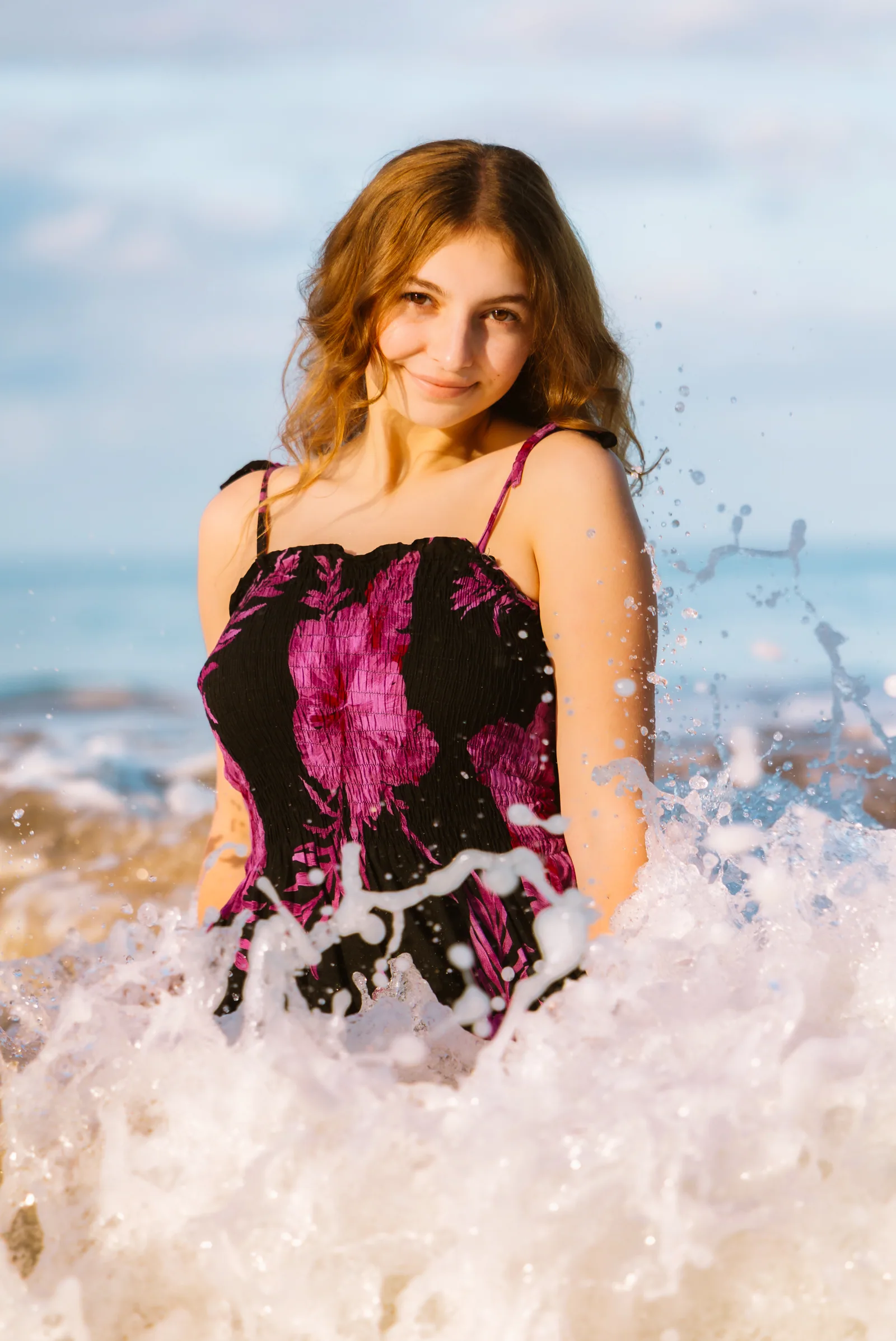 A senior portrait as a wave breaks around her at the shoreline
