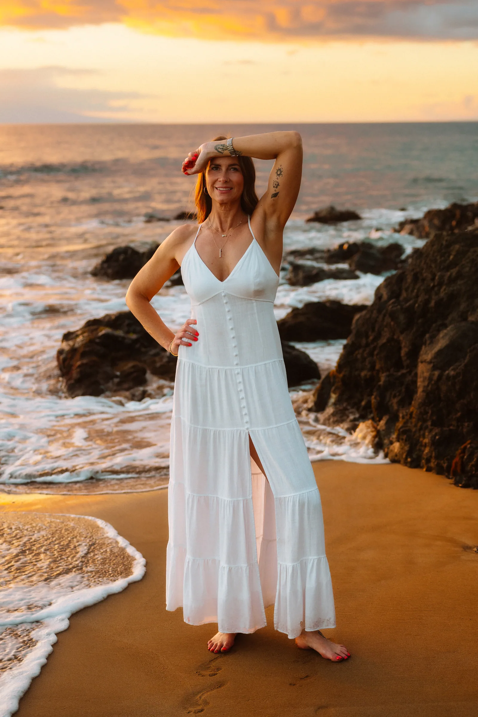 A senior portrait in a white dress on the sand at sunset