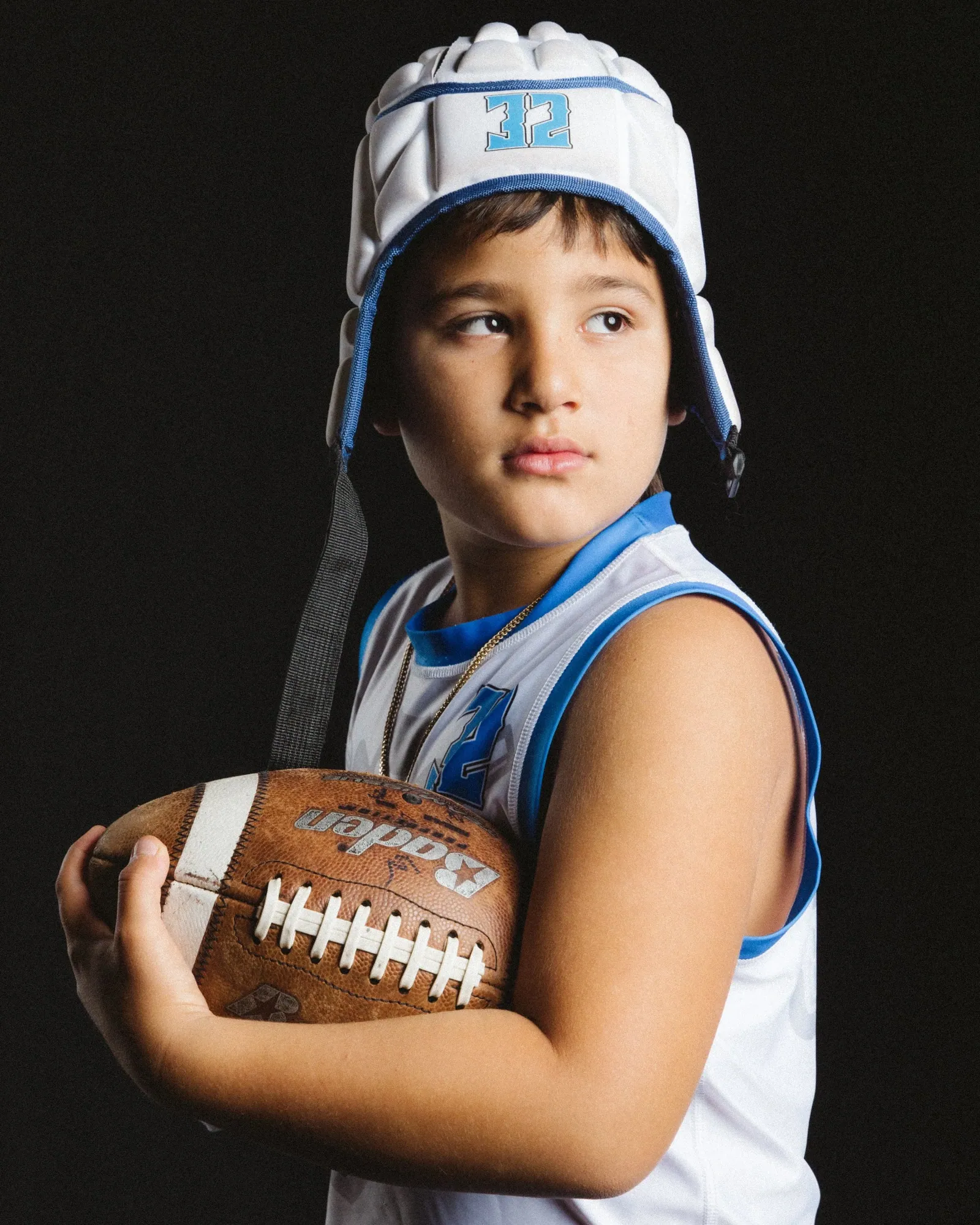 Young football player in his helmet holding the ball, studio portrait on black