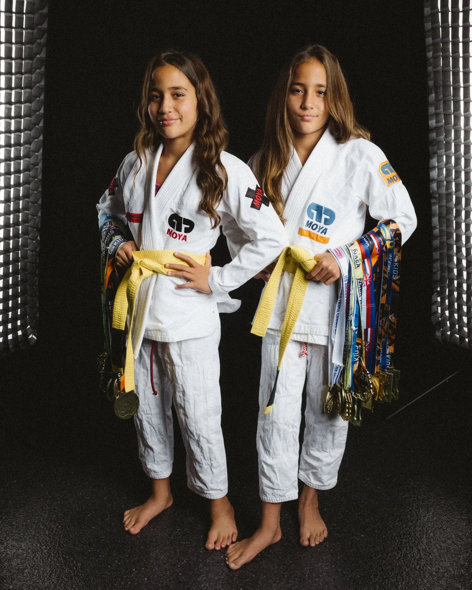 Sisters in their jiu-jitsu gi holding their yellow belts and medals in the studio