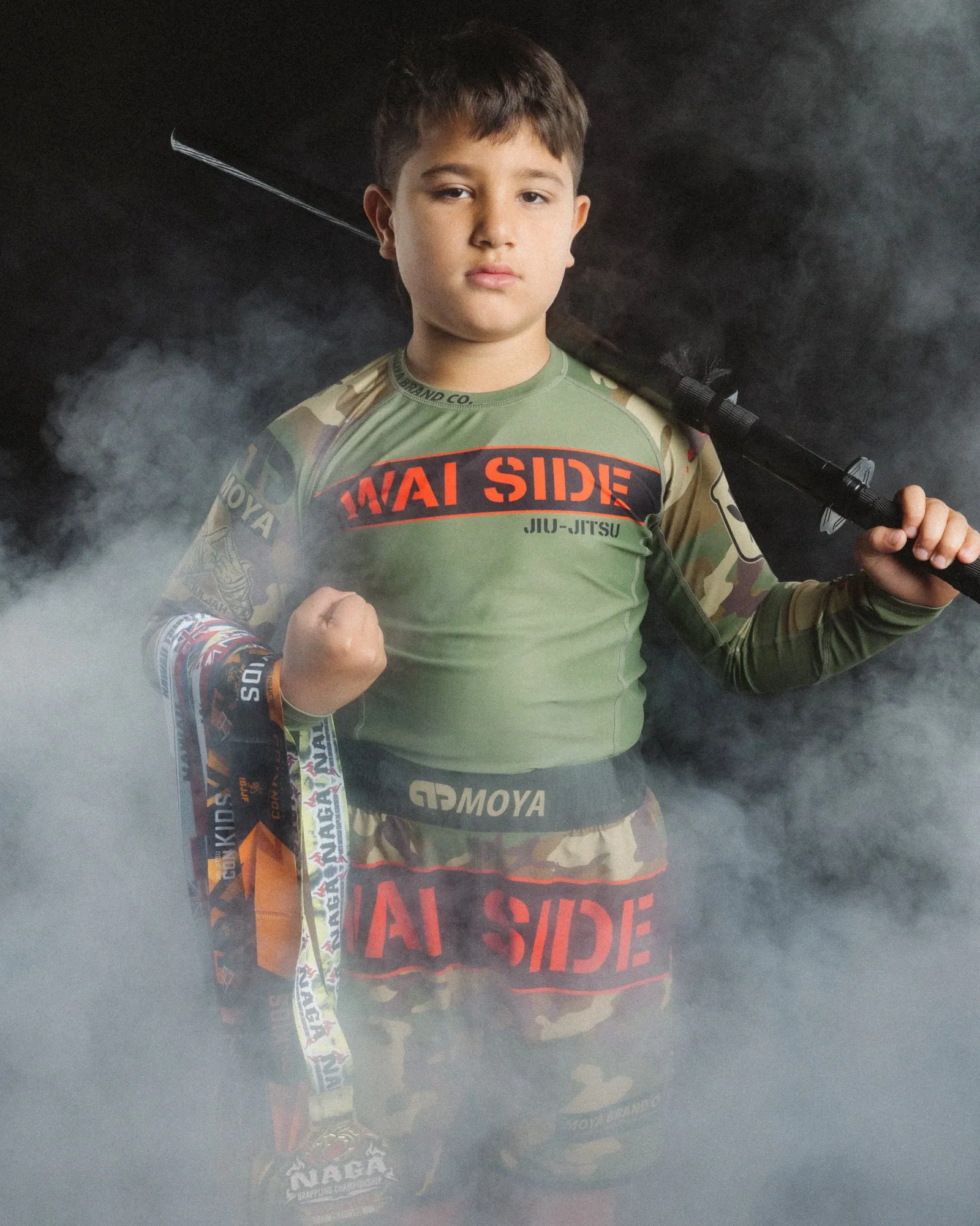 Young athlete with his stick over his shoulder and his medals, studio smoke against black