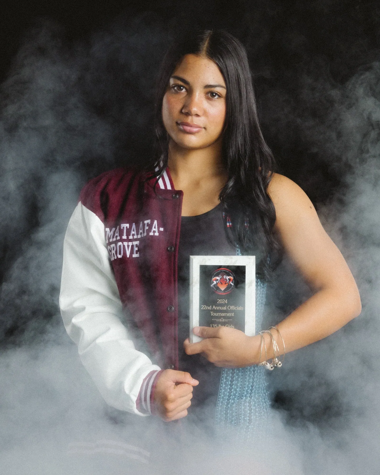 Senior in her letterman jacket holding a tournament plaque, studio smoke against black