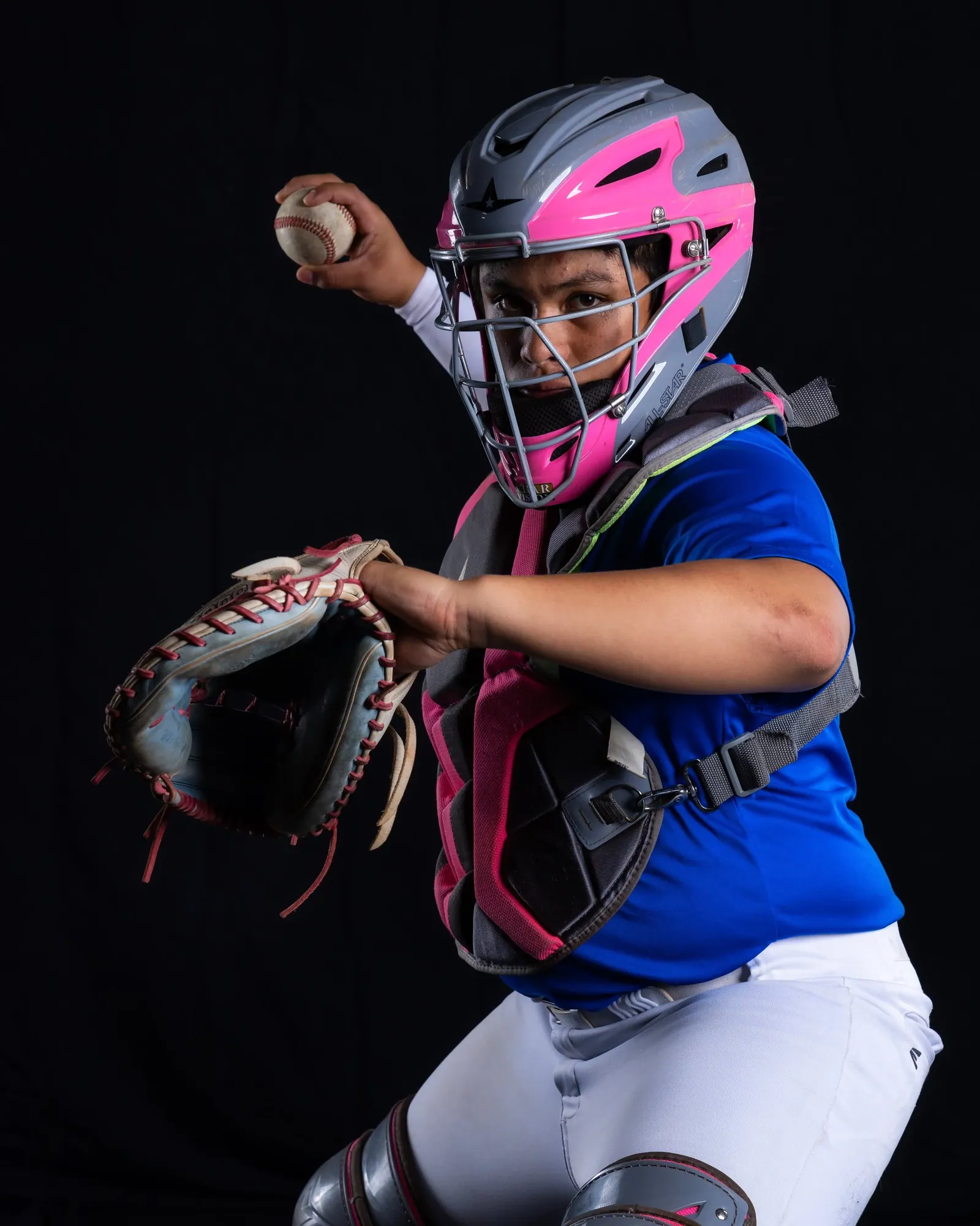 Softball catcher in full gear winding up to throw, studio portrait on black