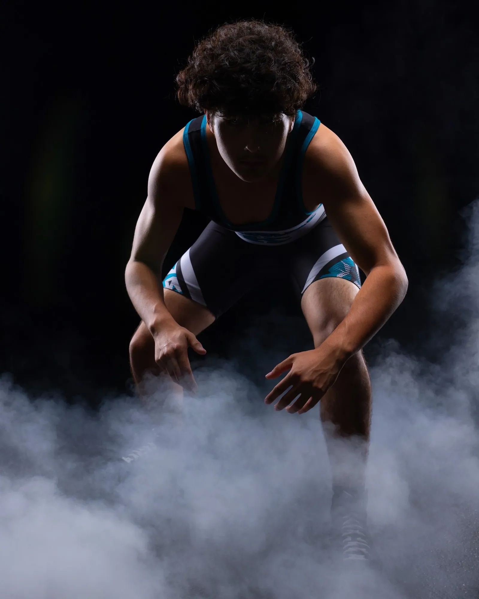 Wrestler crouched in his singlet, heavy studio smoke against black